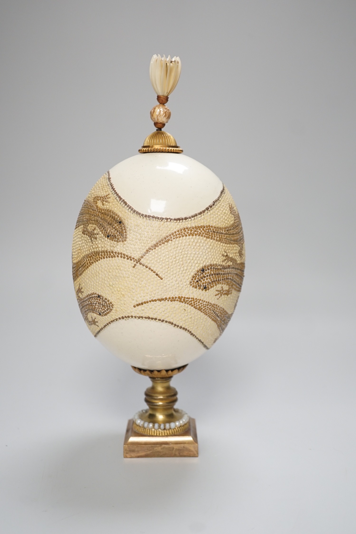 A decorated ostrich egg on gilt stand with a gilt and seed finial, 27cms high